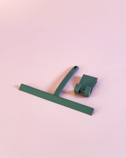 Grauer Silikon-Duschabzieher mit Aufhängevorrichtung vor modernem rosa Hintergrund.