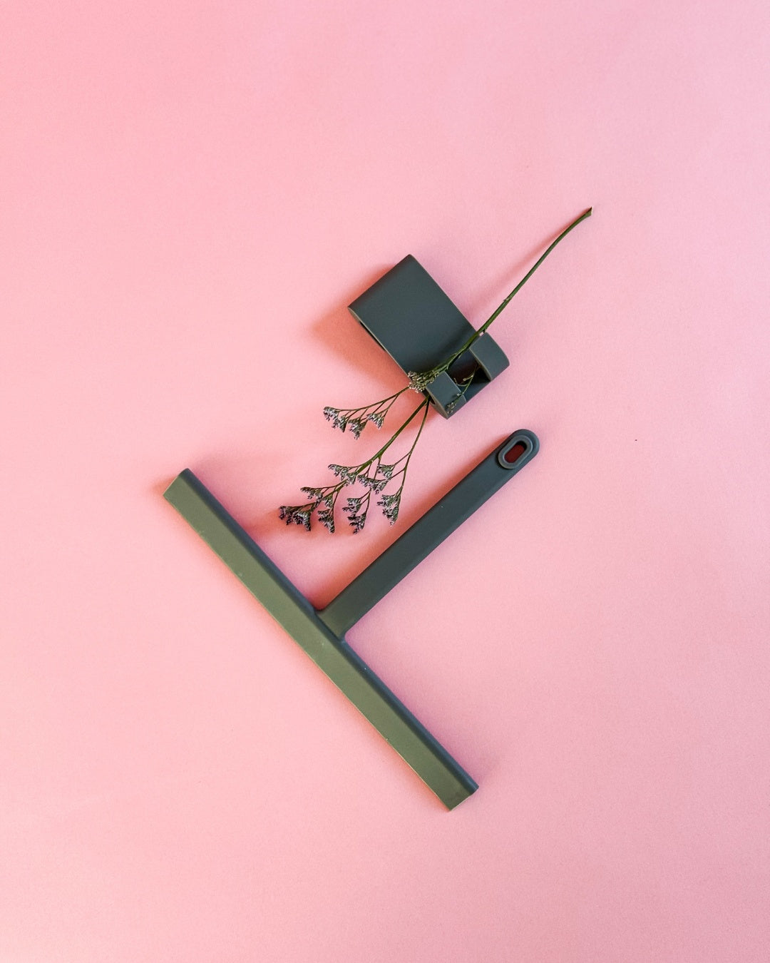 Von oben fotografierter grauer Silikon-Duschabzieher mit Haken und dekorativer Blume.