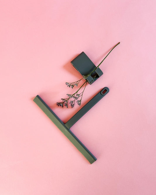 Von oben fotografierter grauer Silikon-Duschabzieher mit Haken und dekorativer Blume.